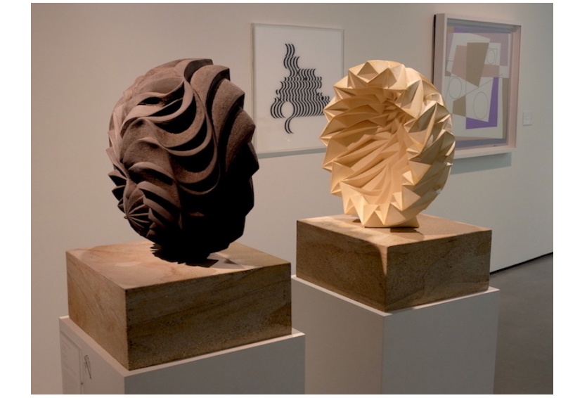 two sculptures, one brown and one cream facing each other in an exhibition 